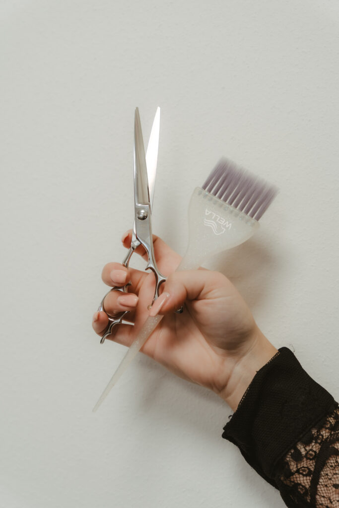 Detailaufnahme einer Hand mit Friseurschere und Pinsel